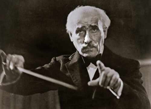 Dirijorul Arturo Toscanini cu bagheta ridicată, portret alb-negru de epocă, privind direct spre obiectiv